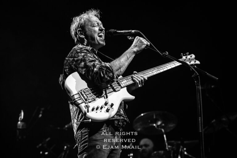 Een muzikant in een zwart-wit afbeelding speelt enthousiast op een basgitaar tijdens een optreden.