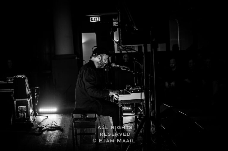 Een muzikant speelt een keyboard op een podium in een gedimde setting.