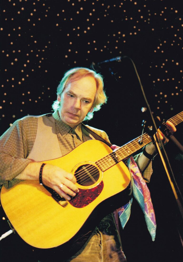 Een muzikant speelt gitaar op een podium met een sterrenachtige achtergrond.