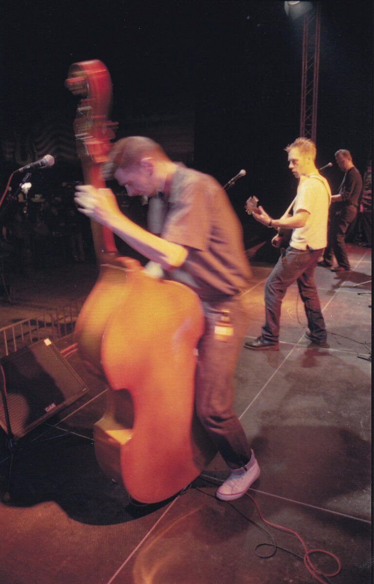 Een band speelt live op het podium, met een muzikant die een contrabas bespeelt.