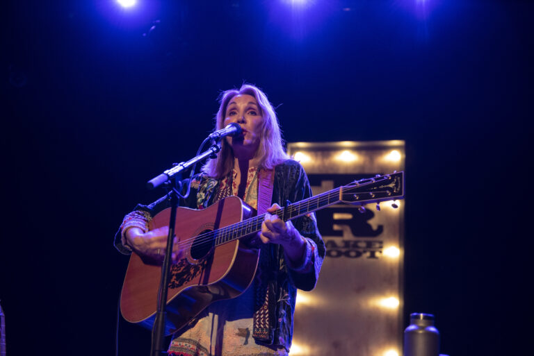 Een muzikant met een gitaar zingt in een sfeervolle lichtsetting op het podium.