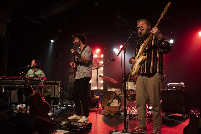 Een band speelt live op een podium met verschillende instrumenten en kleurrijke verlichting.