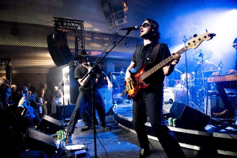 Een band speelt live op een podium met kleurrijke verlichting.