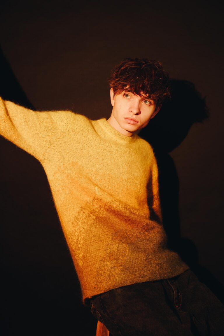 Jongen in gele trui voor een donkere achtergrond