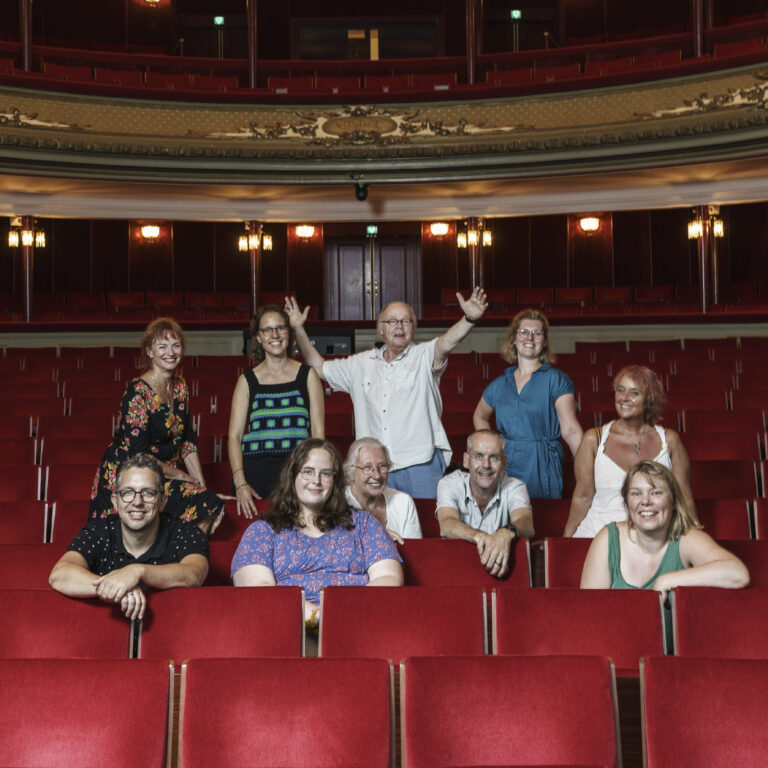 Een groep mensen poseert vrolijk in een theater met rode stoelen.