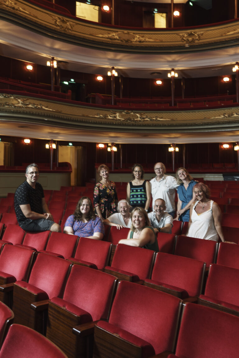 Groep mensen poseert op de rode stoelen in een theater.