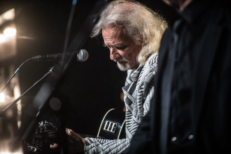 Een muzikant speelt gitaar terwijl hij geconcentreerd naar beneden kijkt.