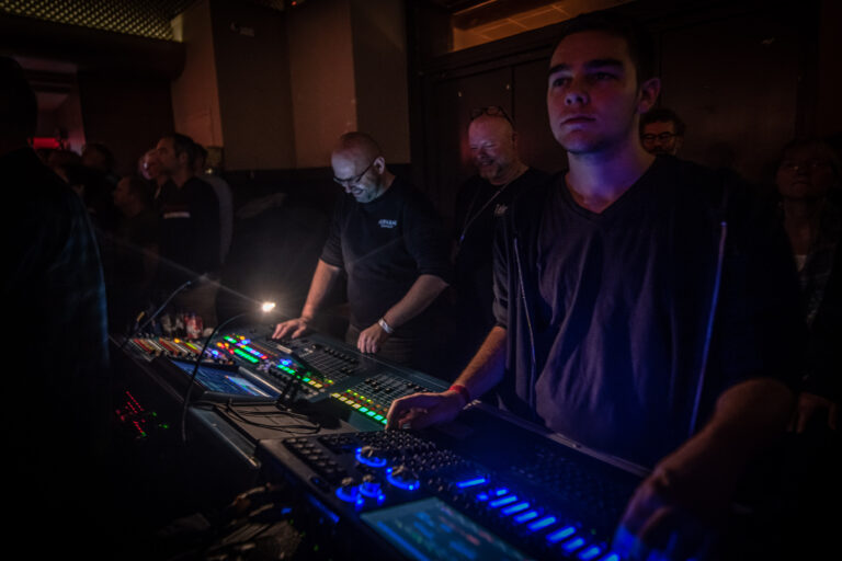 Een groep technici bedient digitale mengpanelen met kleurrijke lichtpanelen in een donkere ruimte.