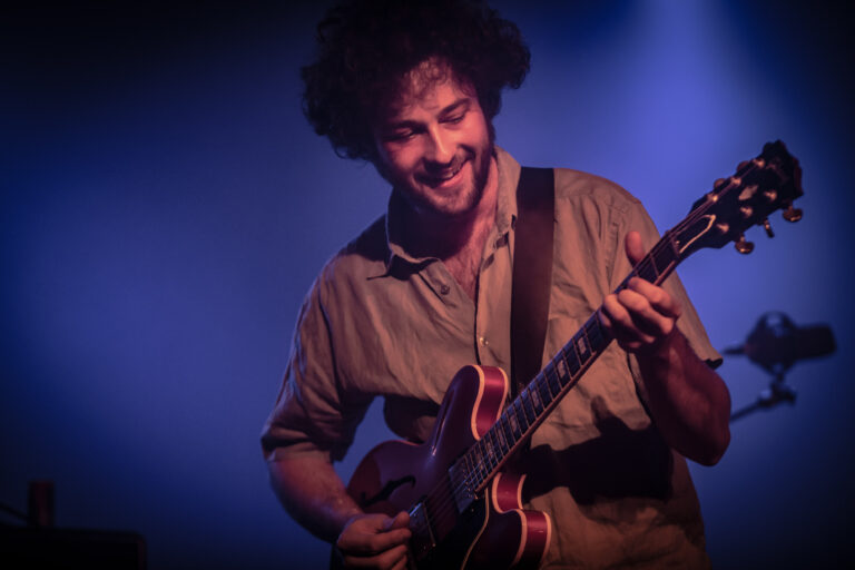 Een man speelt met een gitaar op een podium, omringd door sfeervolle verlichting.