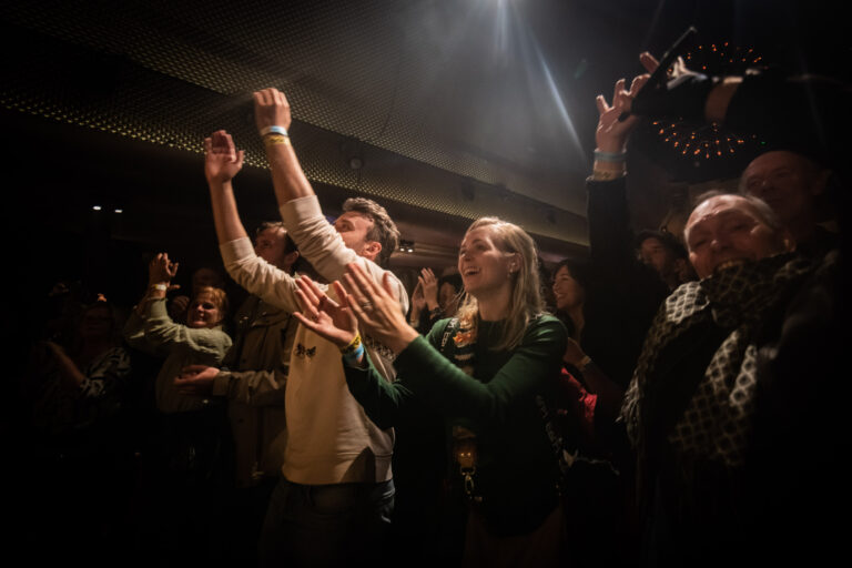 Mensen genieten van een live optreden en vallen in de muziek met opgeheven handen.