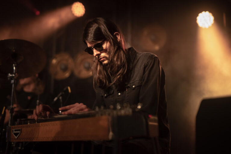 Een muzikant speelt een elektromechanisch instrument op een sfeervol verlicht podium.