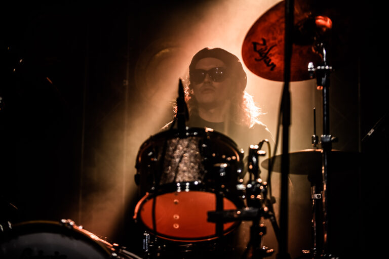 Een drummer speelt op een set met een felgekleurde snaredrum, verlicht door dramatisch licht.