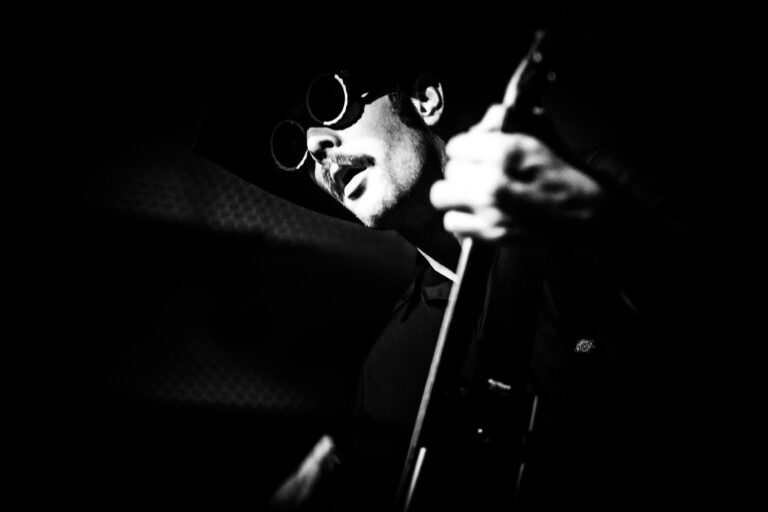 Zwart-wit afbeelding van een muzikant die een gitaar speelt en zonnebril draagt.