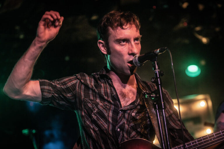 Een muzikant zingt vol enthousiasme in een dimverlichte omgeving met een microfoon in de hand.