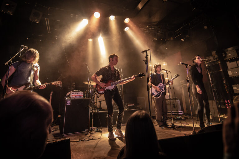 Een band speelt live op het podium met sfeervolle verlichting en rook.