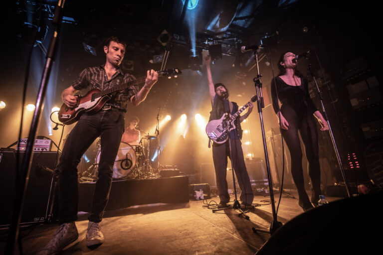 Een live band speelt op een podium met dramatische verlichting en energieke muzikanten.