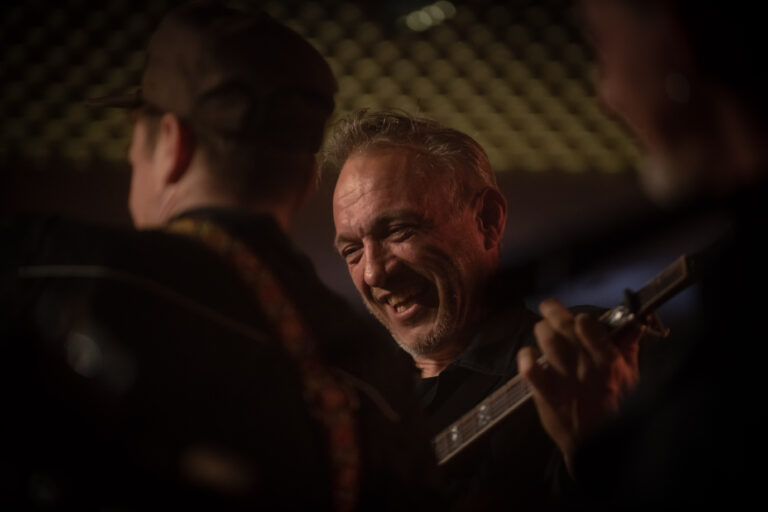 Een glimlachende man speelt gitaar in een intieme muzikale setting.