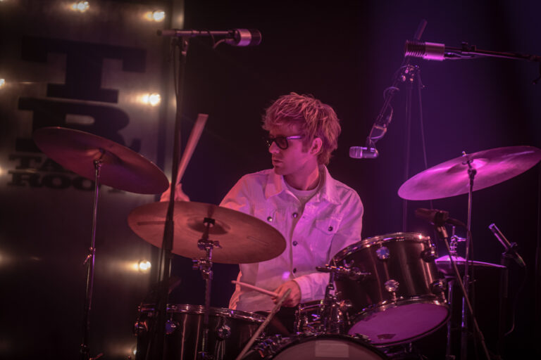 Een drummer speelt op een podium met kleurrijke verlichting.