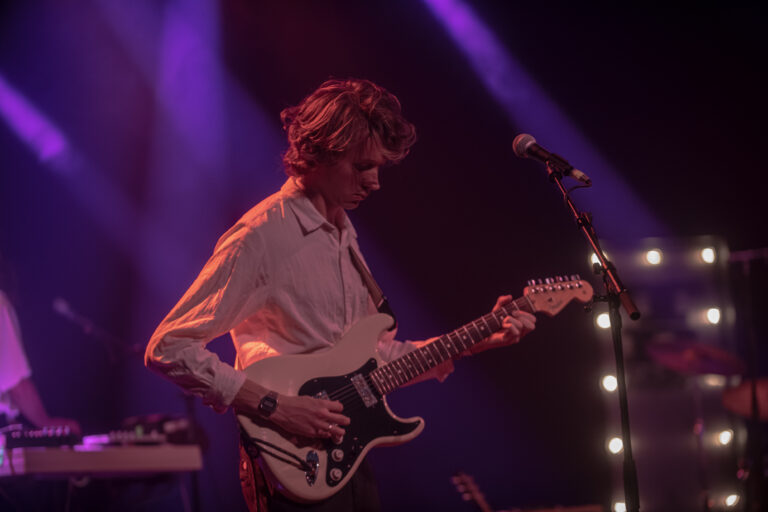 Een muzikant speelt gitaar op het podium, omringd door kleurrijke verlichting.