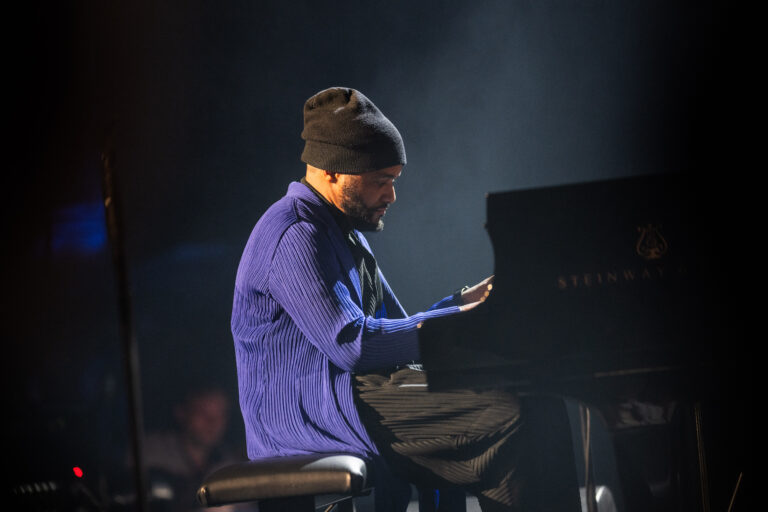 Een muzikant speelt piano op het podium met een lichteffect op de achtergrond.