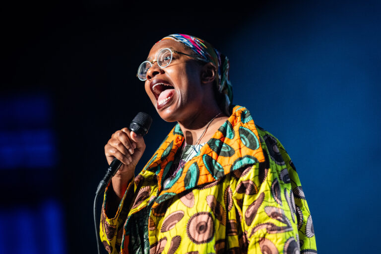 Een zangeres in een kleurrijke outfit houdt een microfoon vast en zingt vol passie op het podium.