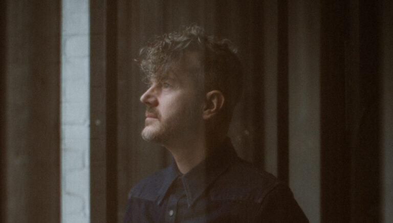 Pianist en componist Delange en profile in een donkerbruine kamer kijkend uit het raam.