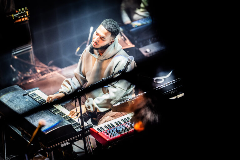 Een muzikant speelt op een piano en synthesizer tijdens een live optreden.