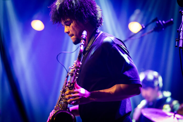Een muzikant speelt saxofon op een podium met kleurrijke verlichting.