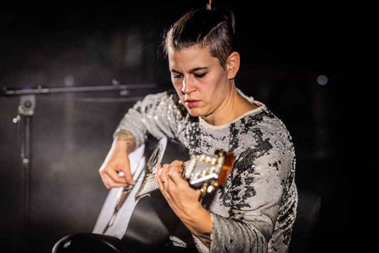 Een muzikant speelt een akoestische gitaar op een donkere, sfeervolle achtergrond.