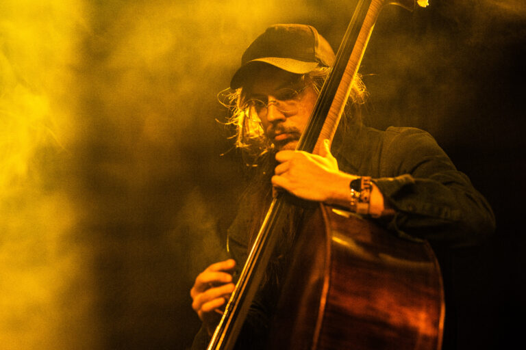 Een muzikant speelt een contrabas terwijl een gele gloed om hem heen hangt.
