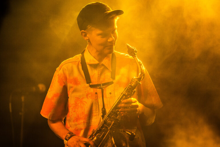 Een muzikant speelt op een saxofoon in een sfeervolle, mistige omgeving met gouden verlichting.