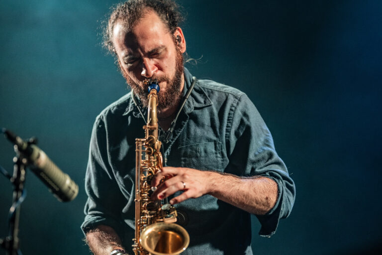 Een muzikant speelt een saxofon op het podium met een blauwe achtergrond.