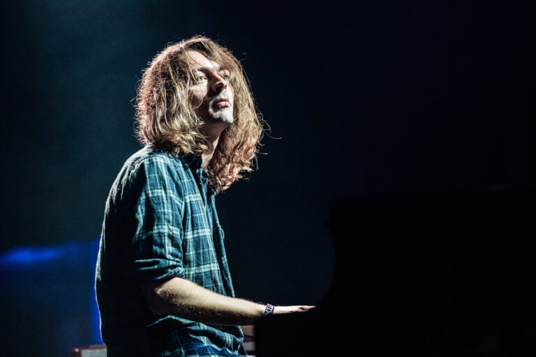 Een muzikant met lang, vol haar speelt enthousiast piano op het podium.