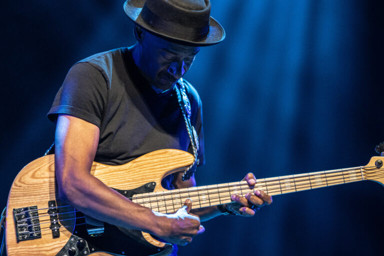 Een muzikant speelt op een elektrische basgitaar onder blauwe lichtstralen.