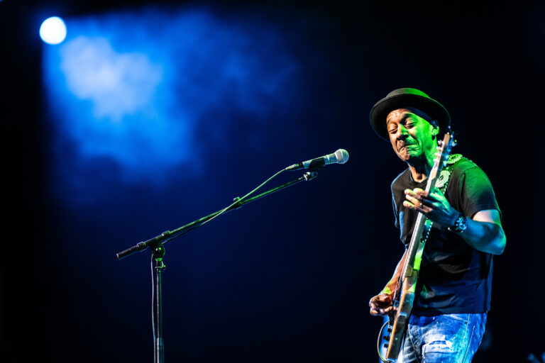 Een muzikant speelt gitaar op een podium met blauwe verlichting.