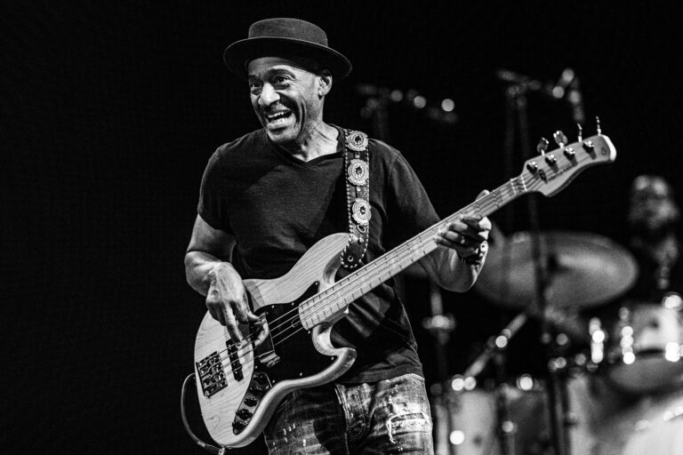 Een muzikant die met een grote glimlach basgitaar speelt op een podium.