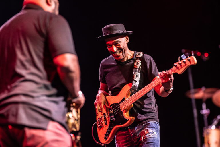 Een muzikant speelt gitaar op het podium terwijl hij naar een andere muzikant kijkt.
