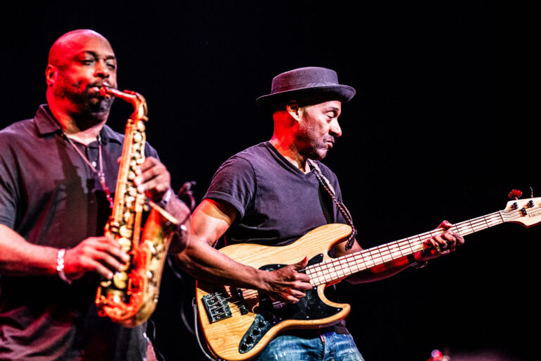 Twee muzikanten spelen op het podium, één met een saxofoon en de ander met een gitaar.