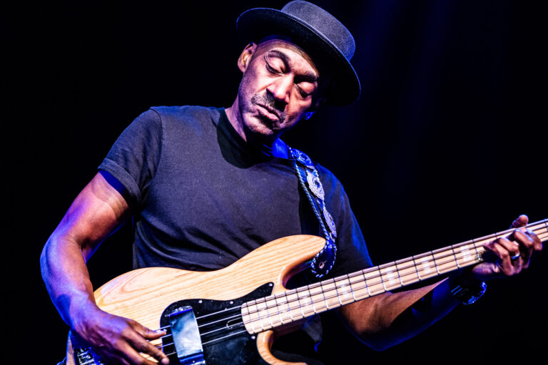 Een muzikant speelt geconcentreerd op een elektrische basgitaar tijdens een optreden.