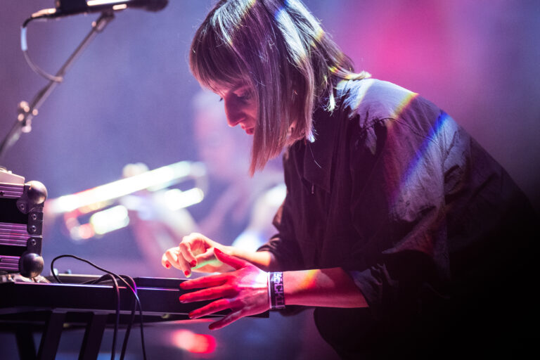 Een muzikant bedient een toetsenbord terwijl kleurrijke lichten op de achtergrond stralen.
