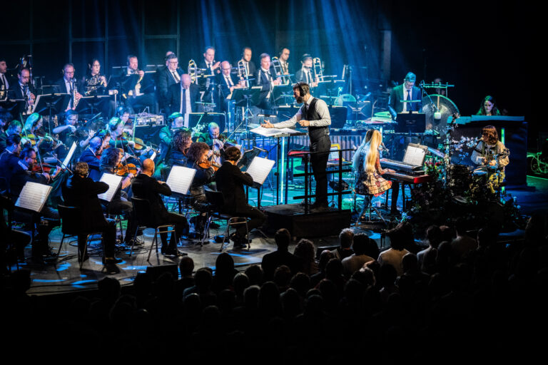 Een live orkest speelt op een podium met een dirigent voor een publiek in een sfeervolle setting.