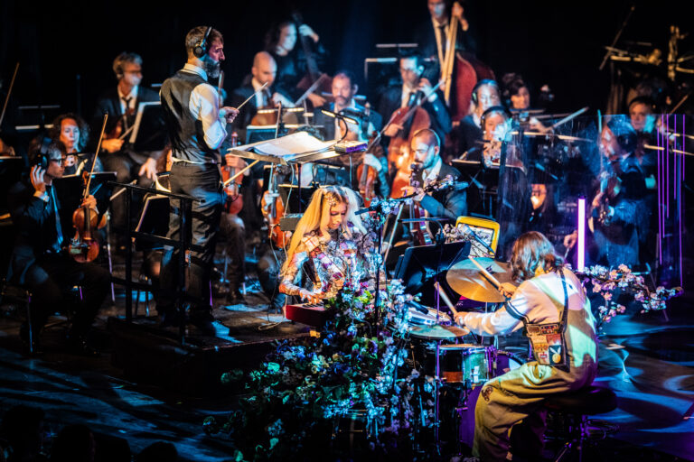 Een orkest bestaat uit verschillende muzikanten die samen op een podium optreden, met een nadruk op ritmes en instrumenten.