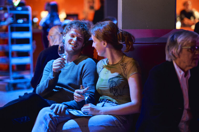 twee mensen die naar elkaar lachen met een glas wijn in de hand.