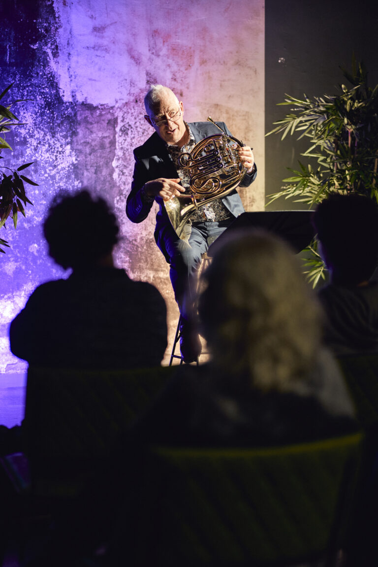 Oudere man met een blaasinstrument in zijn handen.