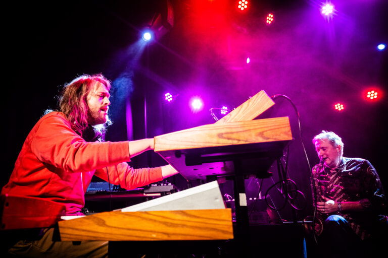 Een muzikant speelt op een keyboard met kleurrijke lichten op de achtergrond.