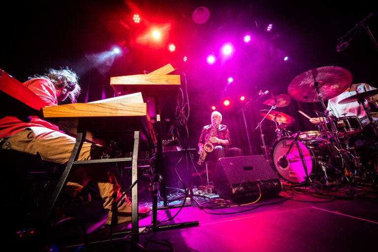 Een muzikale band speelt live op een podium met kleurrijke verlichting.