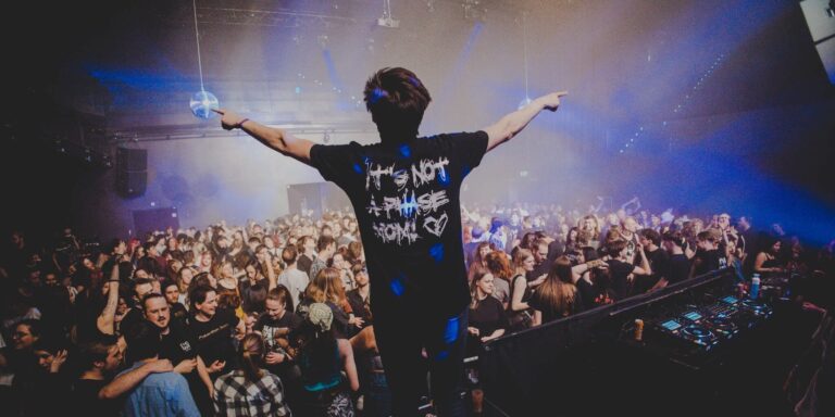 Een man die boven op een DJ-booth staat met zijn armen wijd