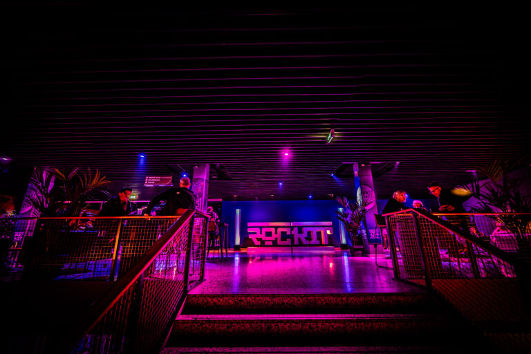 Een uitgelichte dansvloer met kleurrijke verlichting en een opvallend bord met de naam