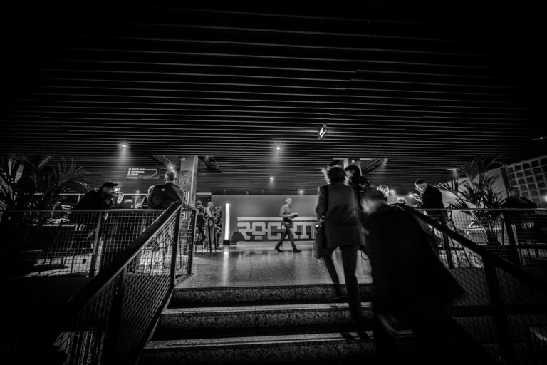 Mensen lopen naar beneden via een trap in een donkere, verlichte ruimte met moderne architectuur.