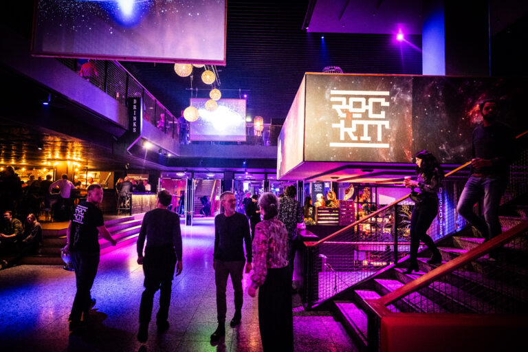 Een levendige binnenruimte van een nachtclub met kleurrijke verlichting en mensen die zich verplaatsen.